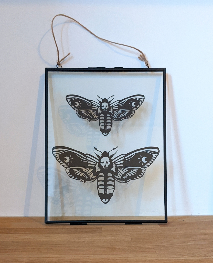 Two framed papercuts of a deaths head moth