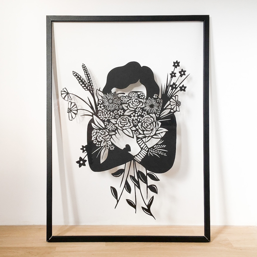 Frame papercut artwork of a woman clutching a huge bouquet